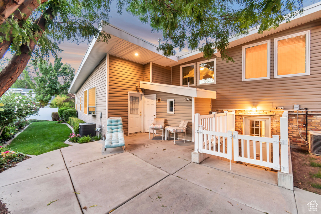 Back house at dusk featuring a patio, central AC, and a lawn