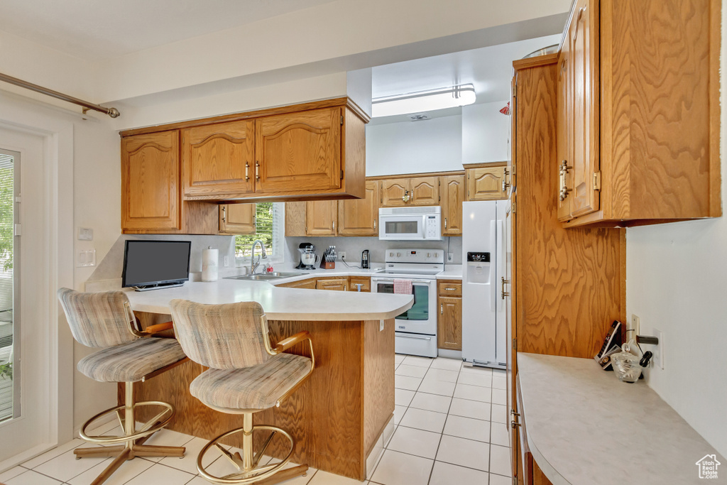 Kitchen featuring a kitchen bar, sink, kitchen peninsula, light tile patterned flooring, and white appliances