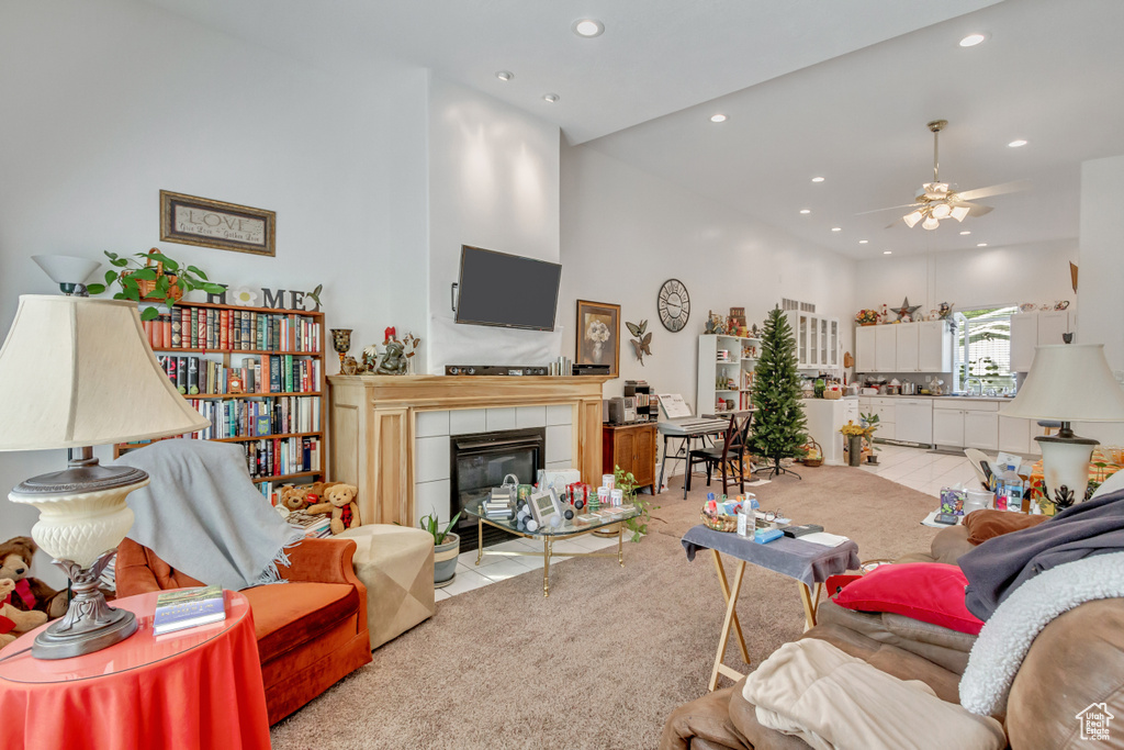 Carpeted living room featuring a fireplace, ceiling fan, and a high ceiling