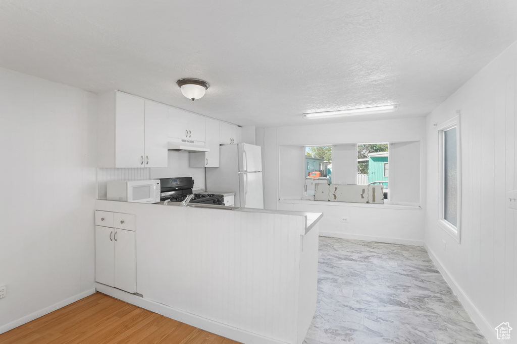 Kitchen with decorative backsplash, white cabinetry, light hardwood / wood-style floors, kitchen peninsula, and white appliances