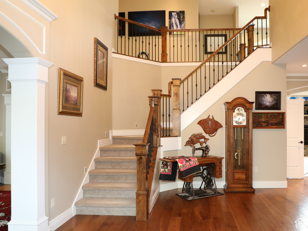 Stairway featuring ornate columns, hardwood / wood-style flooring, and a towering ceiling