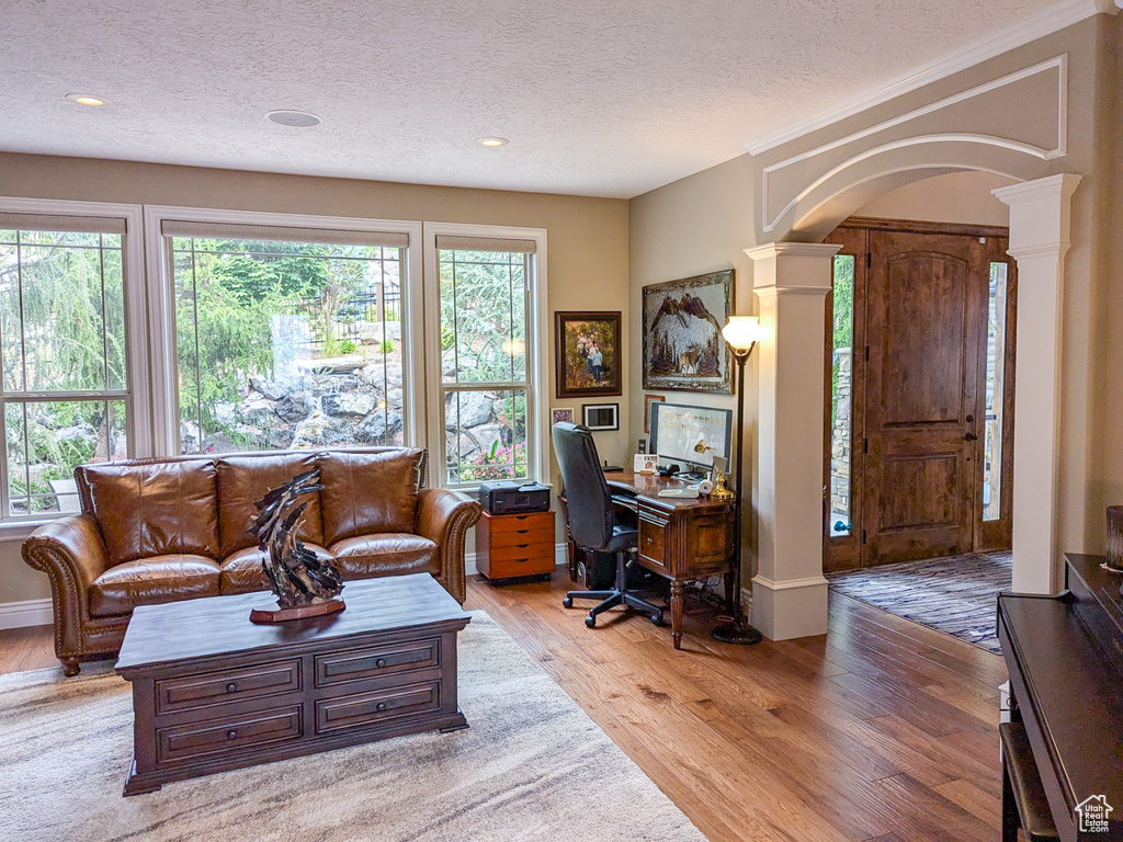 Office space featuring a textured ceiling, light hardwood / wood-style floors, and decorative columns