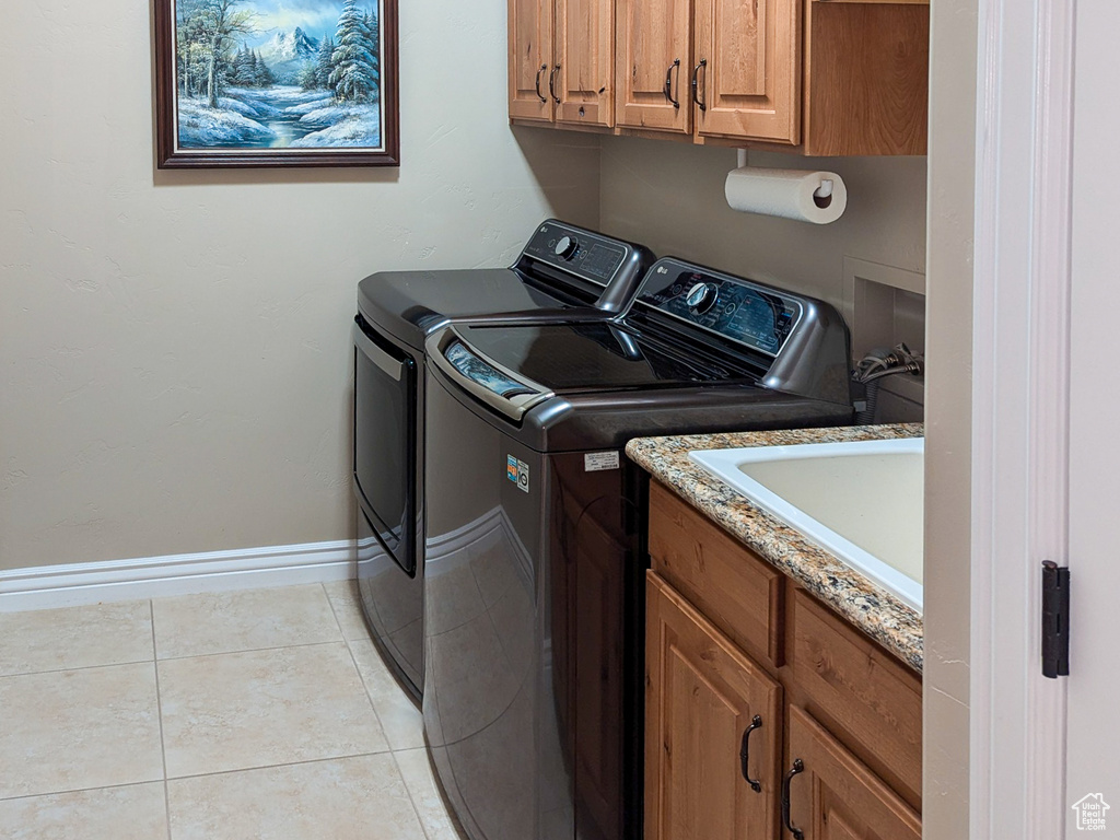 Washroom featuring sink, washing machine and dryer, light tile patterned floors, and cabinets