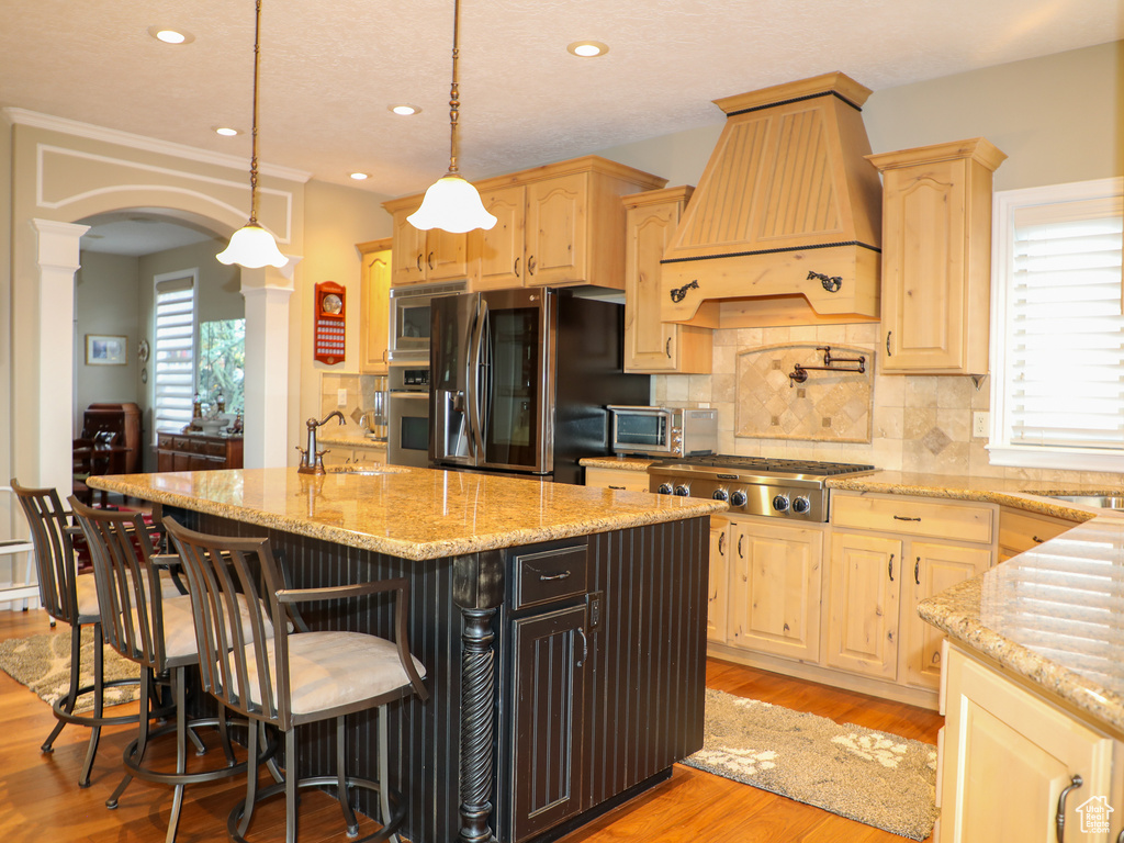 Kitchen featuring decorative backsplash, custom range hood, light hardwood / wood-style floors, decorative light fixtures, and stainless steel appliances