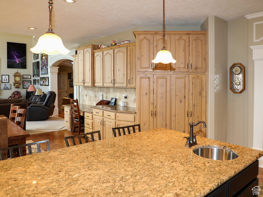 Kitchen featuring backsplash, sink, light wood-type flooring, pendant lighting, and light brown cabinetry