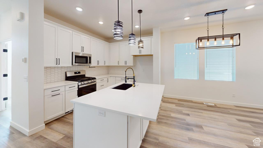 Kitchen with light wood-type flooring, appliances with stainless steel finishes, backsplash, and a center island with sink