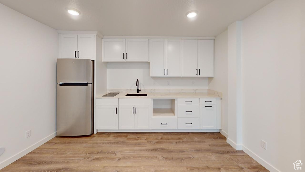 Kitchen with white cabinetry, light hardwood / wood-style floors, stainless steel refrigerator, and sink