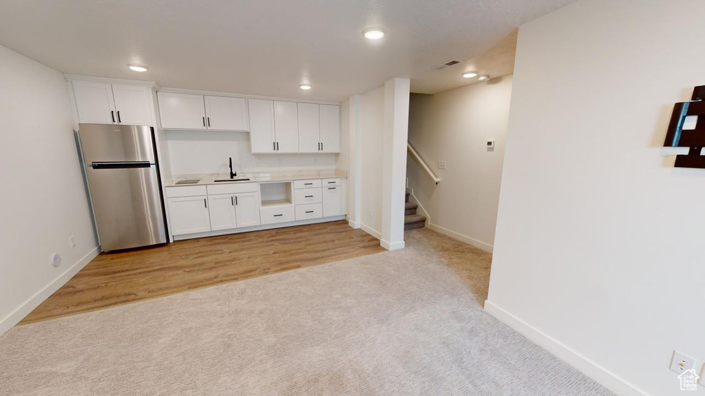 Kitchen featuring light colored carpet, stainless steel refrigerator, sink, and white cabinetry