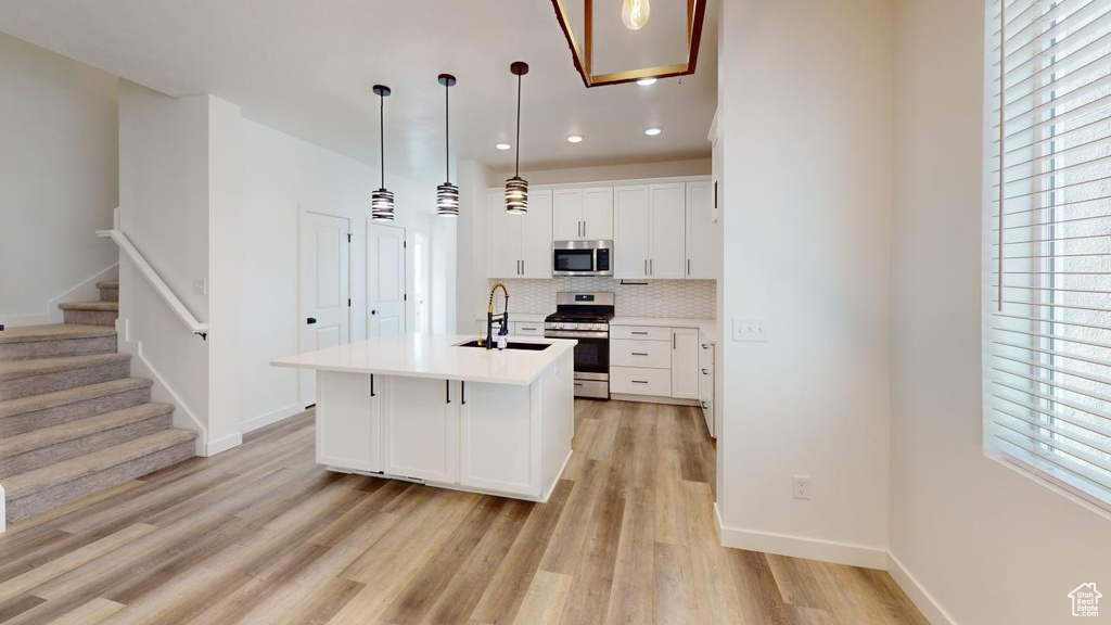 Kitchen with backsplash, light hardwood / wood-style flooring, appliances with stainless steel finishes, white cabinetry, and a center island with sink