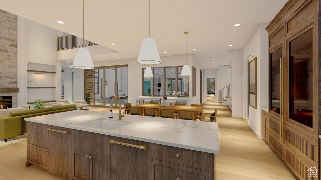 Kitchen with a large island, pendant lighting, light wood-type flooring, sink, and a large fireplace