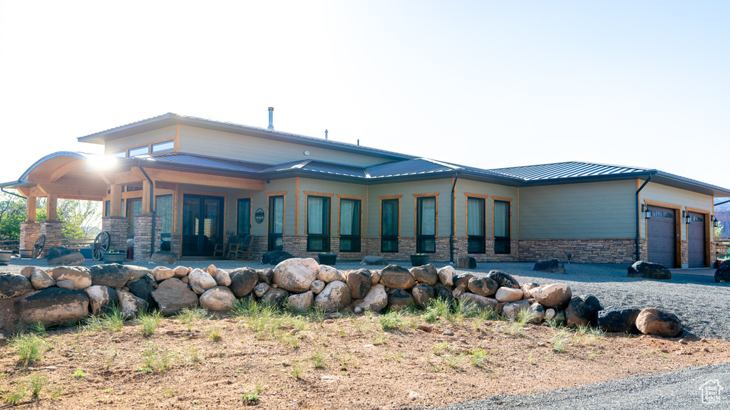 Back of property with stone siding, metal roof, a garage, and a standing seam roof