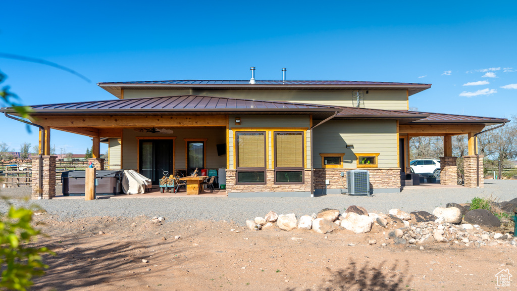 Rear view of house featuring a standing seam roof, a patio, central AC unit, stone siding, and metal roof