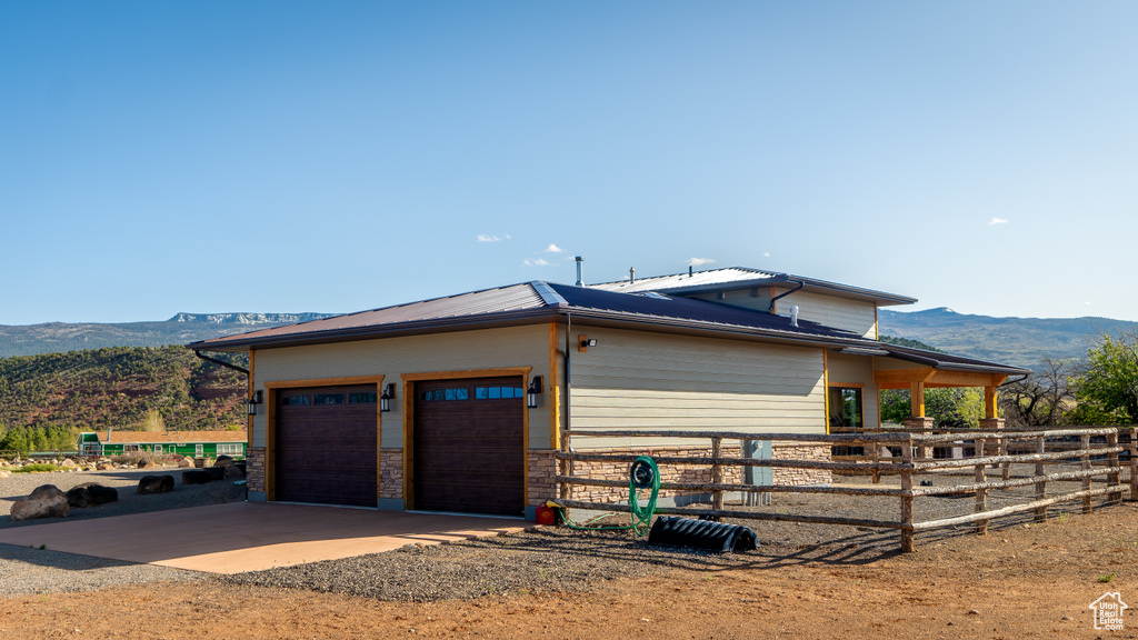 View of side of property with a mountain view, dirt driveway, an attached garage, and metal roof