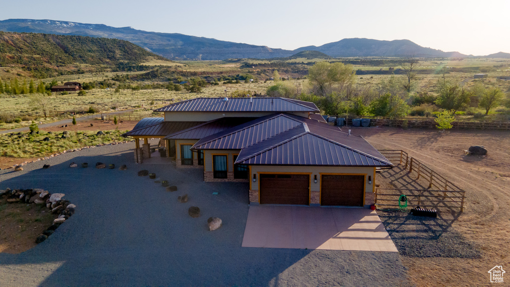 View of front of house featuring a mountain view, fence, an attached garage, metal roof, and driveway
