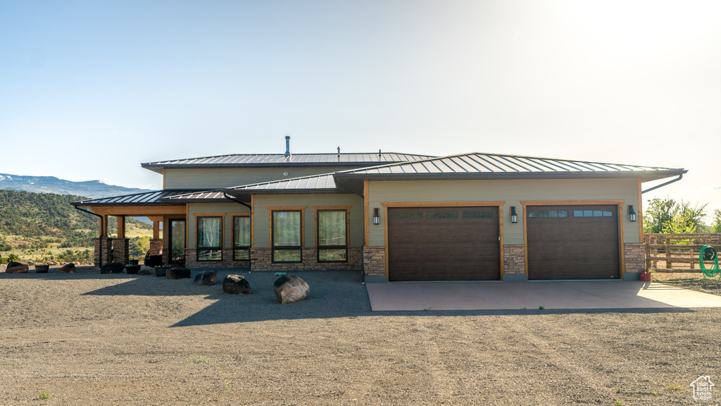 View of front of house with dirt driveway, a standing seam roof, a garage, fence, and a mountain view