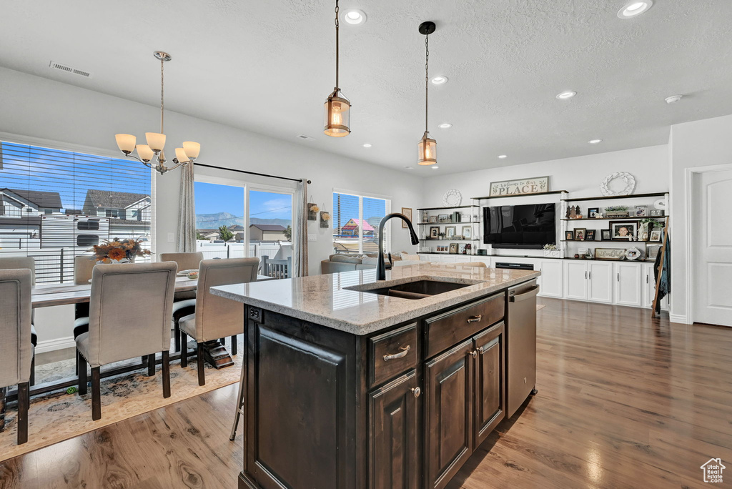 Kitchen featuring a kitchen island with sink, dark wood-type flooring, decorative light fixtures, and sink