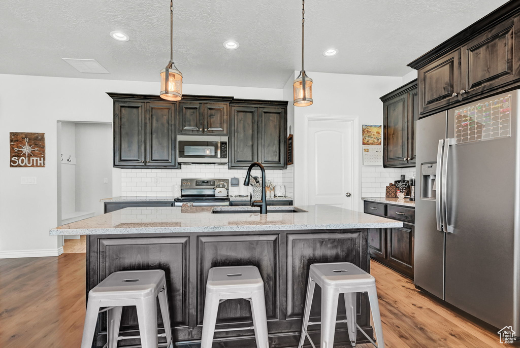 Kitchen with backsplash, stainless steel appliances, sink, and light hardwood / wood-style flooring