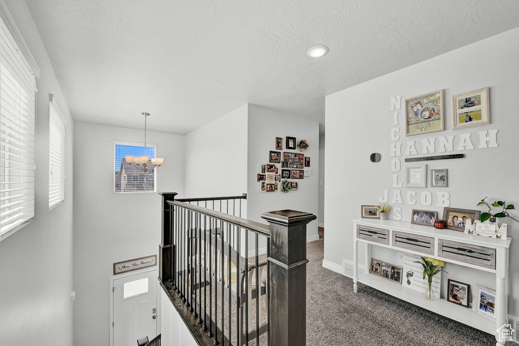 Hallway with dark carpet, plenty of natural light, an inviting chandelier, and a textured ceiling