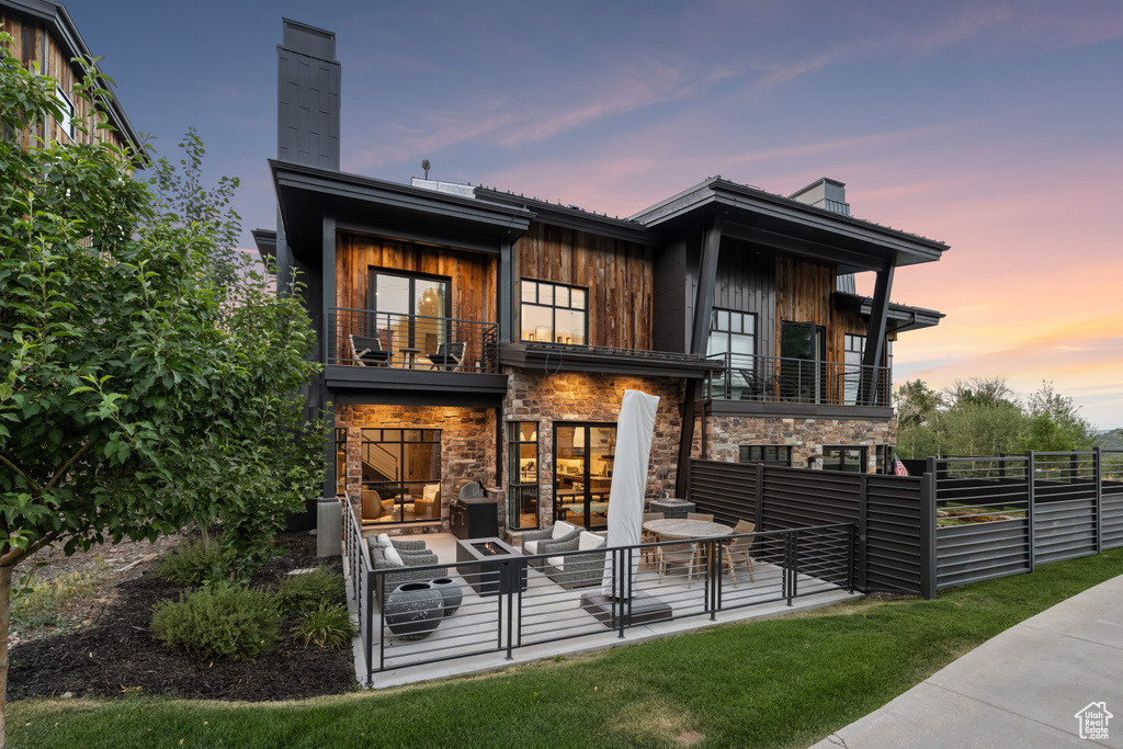 Back house at dusk featuring a balcony and outdoor lounge area