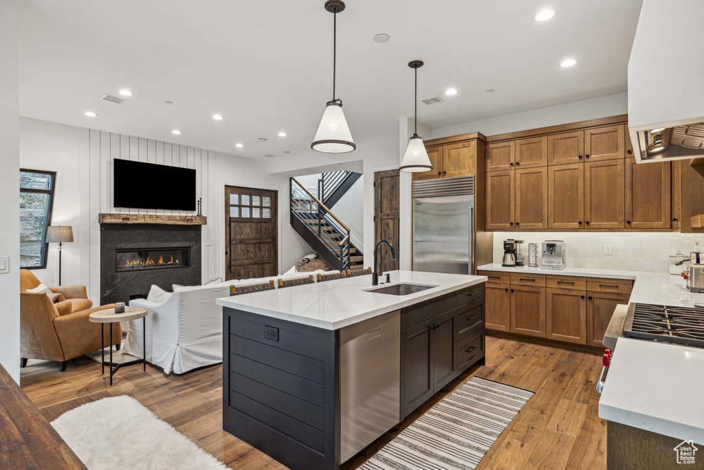 Kitchen featuring light wood-type flooring, decorative light fixtures, a premium fireplace, sink, and decorative backsplash