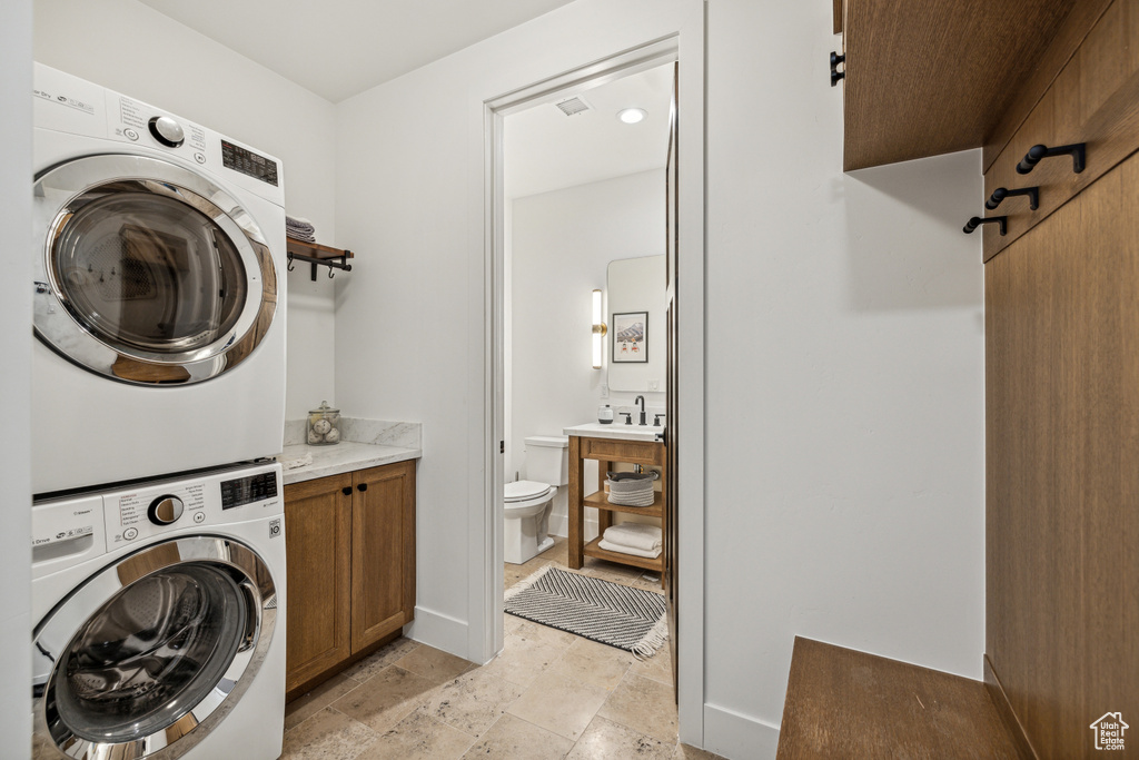 Laundry room with stacked washer and dryer, cabinets, and light tile patterned flooring