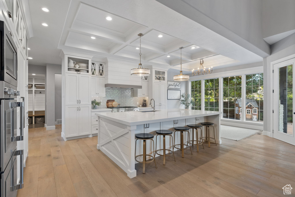 Kitchen with white cabinets, a large island, decorative light fixtures, and light wood-type flooring