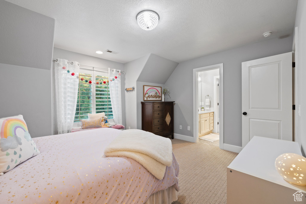 Carpeted bedroom featuring a textured ceiling, lofted ceiling, and ensuite bath