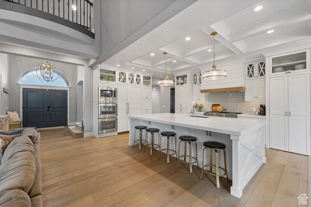 Kitchen with white cabinetry, hanging light fixtures, light hardwood / wood-style flooring, stainless steel appliances, and a spacious island