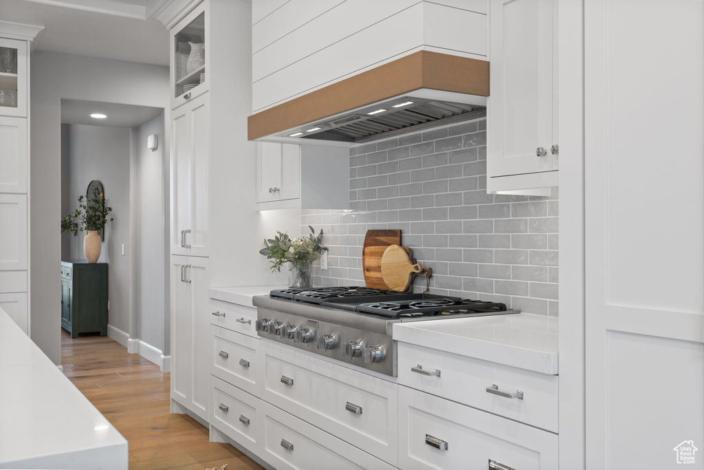 Kitchen with stainless steel gas stovetop, white cabinets, light hardwood / wood-style floors, and tasteful backsplash