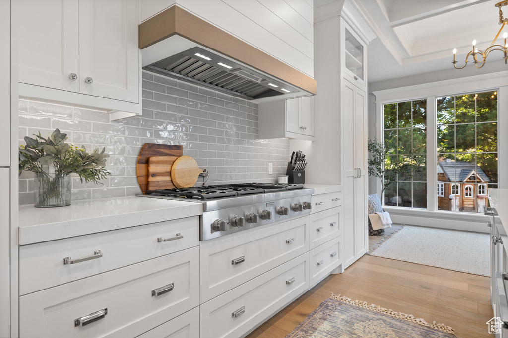 Kitchen featuring light wood-type flooring, custom range hood, stainless steel gas cooktop, and white cabinetry