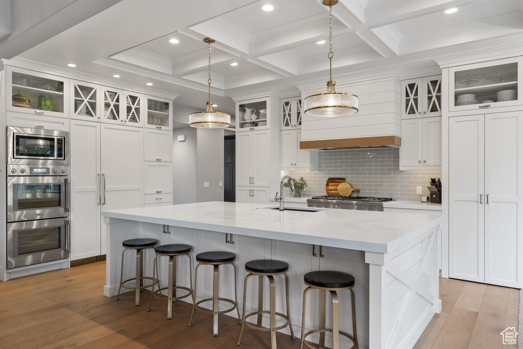 Kitchen featuring coffered ceiling, a large island, light wood-type flooring, decorative light fixtures, and sink