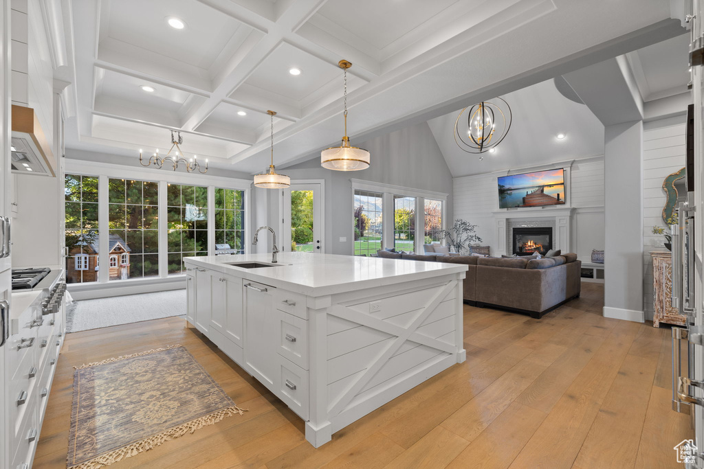 Kitchen featuring light wood-type flooring, an island with sink, white cabinets, hanging light fixtures, and an inviting chandelier