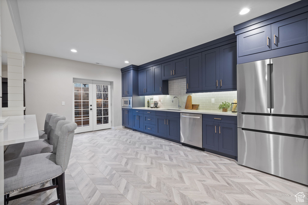 Kitchen featuring blue cabinets, tasteful backsplash, light parquet flooring, built in appliances, and sink