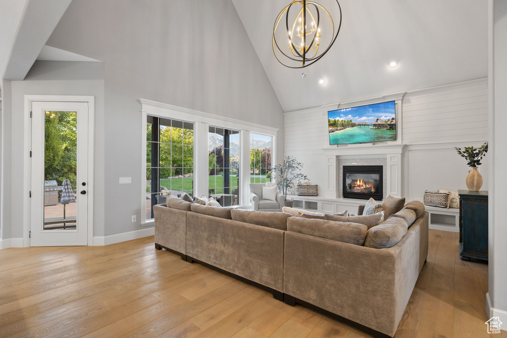 Living room featuring high vaulted ceiling, light wood-type flooring, a chandelier, and a healthy amount of sunlight