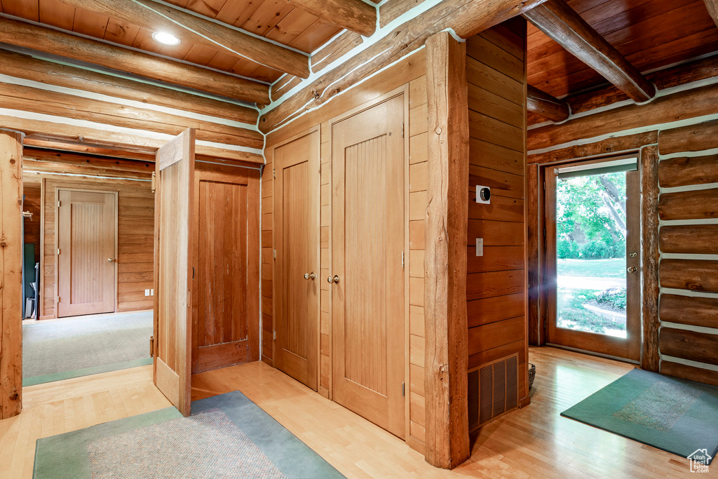 Corridor with wood walls, light hardwood / wood-style floors, beamed ceiling, and wooden ceiling