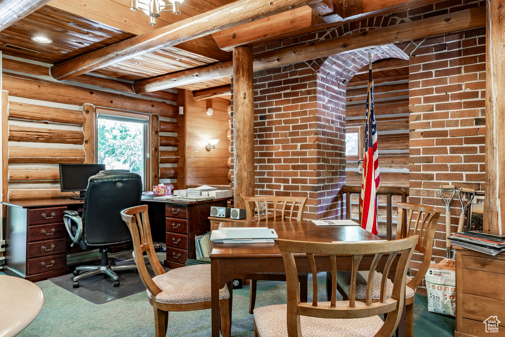 Carpeted office space featuring log walls, brick wall, wooden ceiling, and beam ceiling