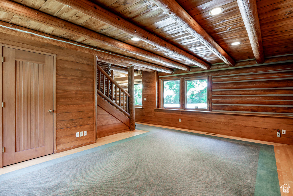 Carpeted empty room featuring wood ceiling, log walls, wooden walls, and beam ceiling