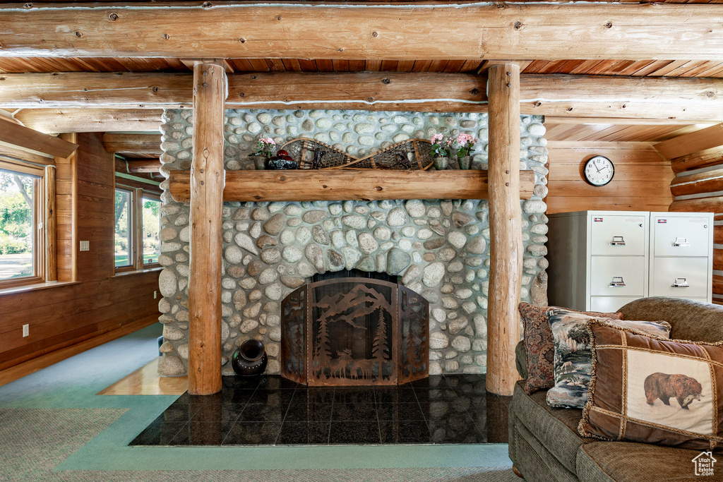 Living room featuring wooden walls, wooden ceiling, beamed ceiling, a stone fireplace, and rustic walls