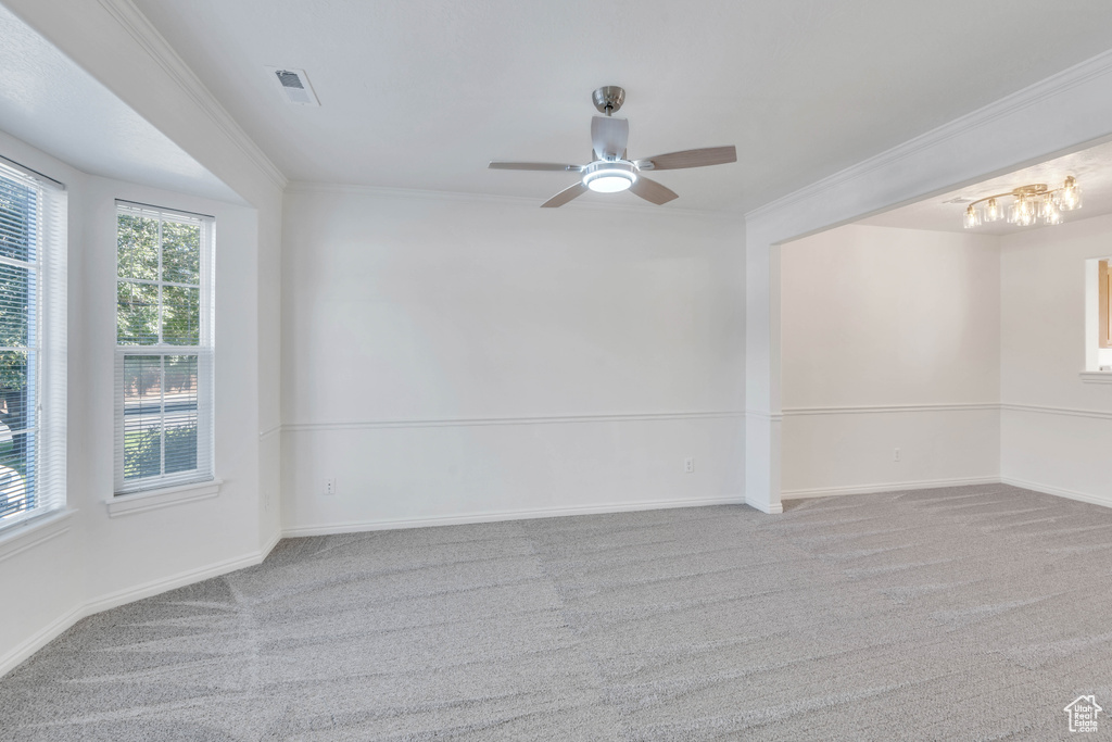 Carpeted spare room featuring ornamental molding and ceiling fan with notable chandelier