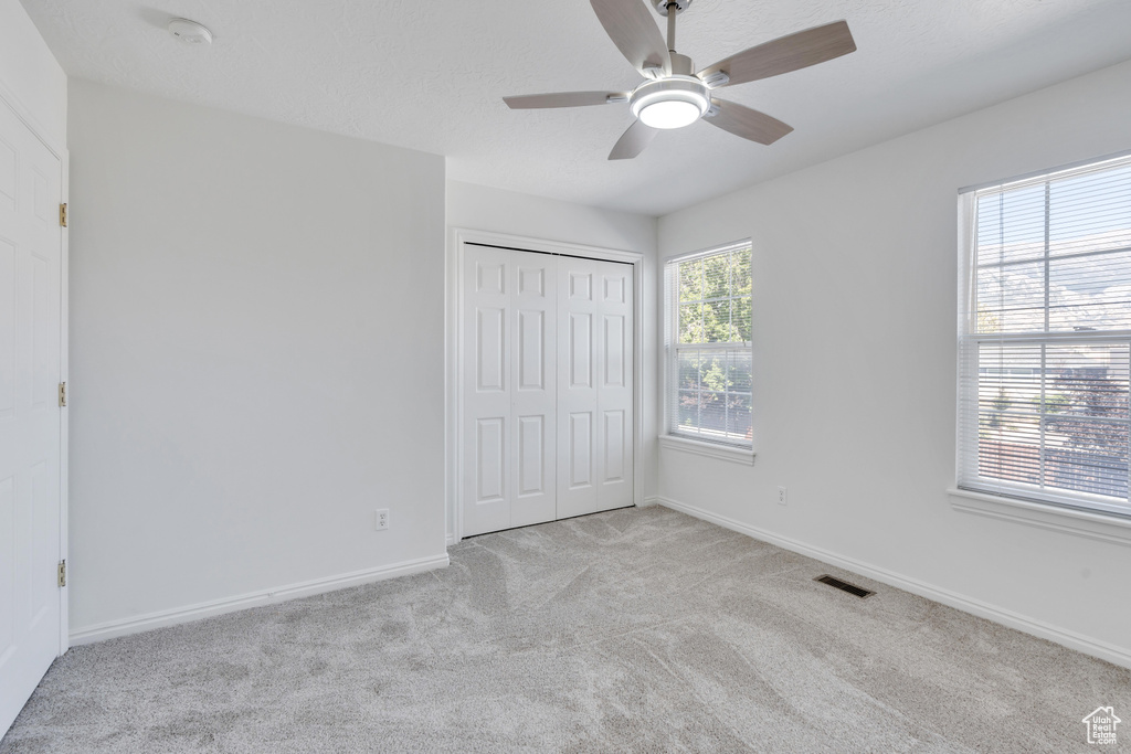 Unfurnished bedroom featuring light colored carpet, ceiling fan, a closet, and multiple windows