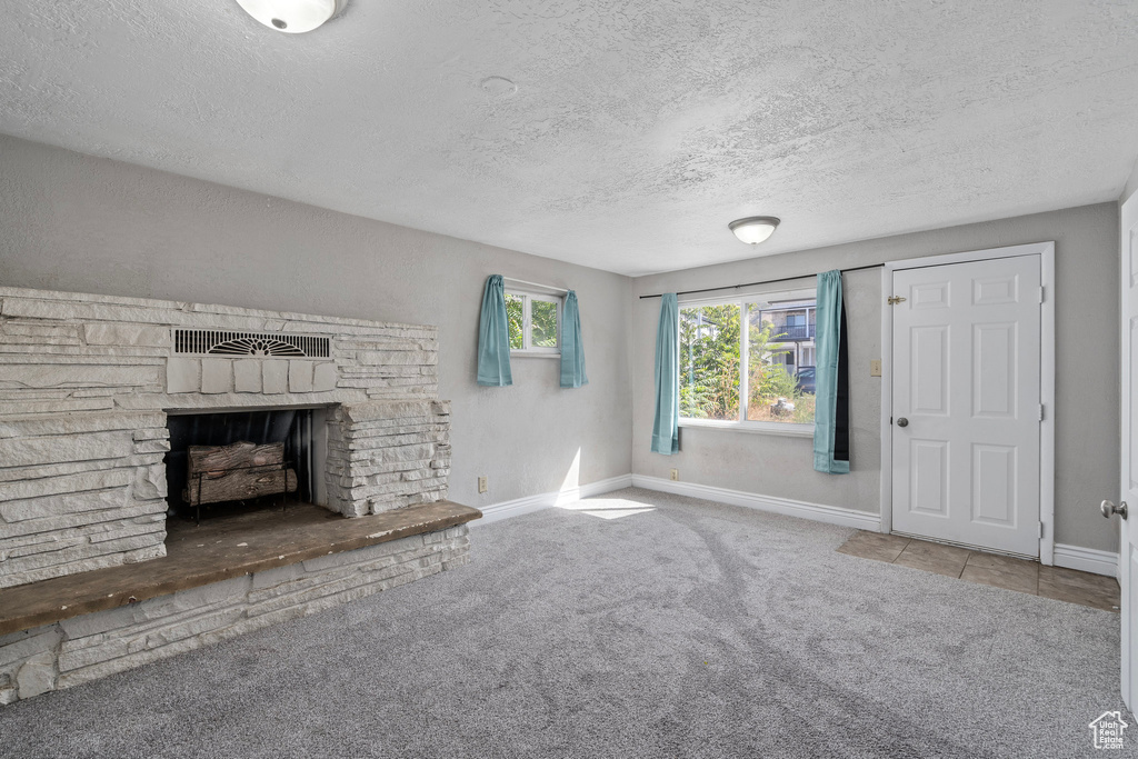 Unfurnished living room featuring carpet floors, a stone fireplace, and a textured ceiling