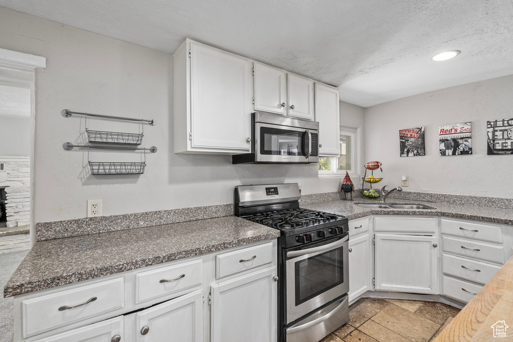 Kitchen featuring light tile patterned floors, sink, stainless steel appliances, and white cabinets