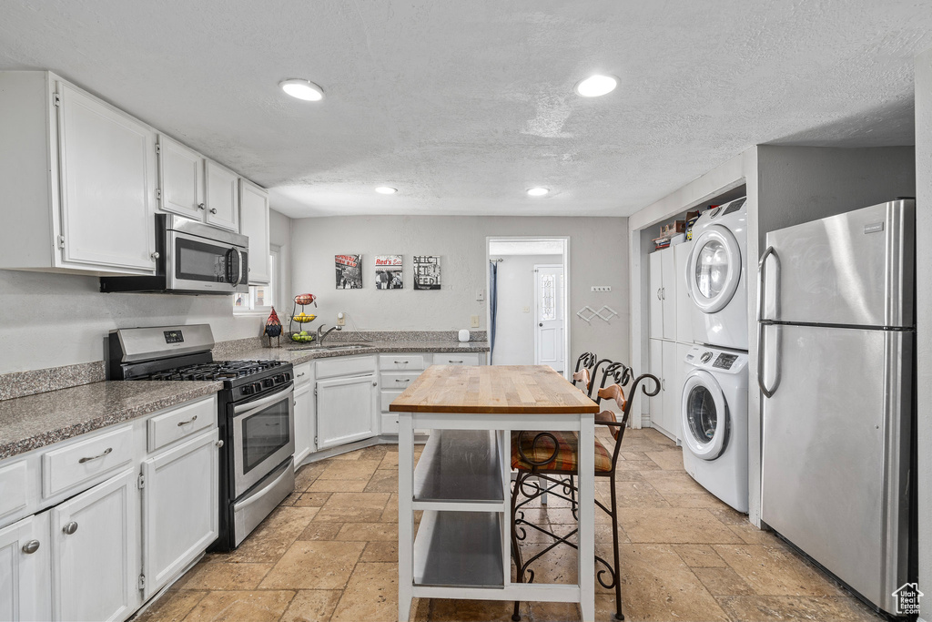 Kitchen with stacked washer / drying machine, sink, white cabinetry, light tile patterned floors, and stainless steel appliances