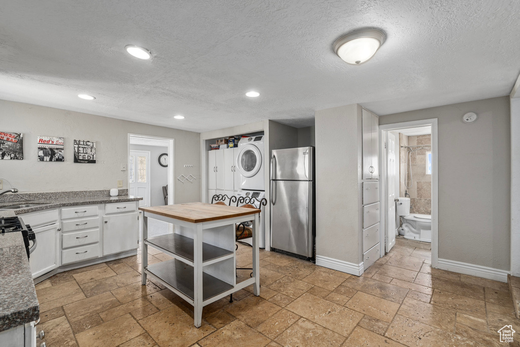 Kitchen featuring white cabinets, stainless steel refrigerator, stacked washer and clothes dryer, light tile patterned floors, and a textured ceiling