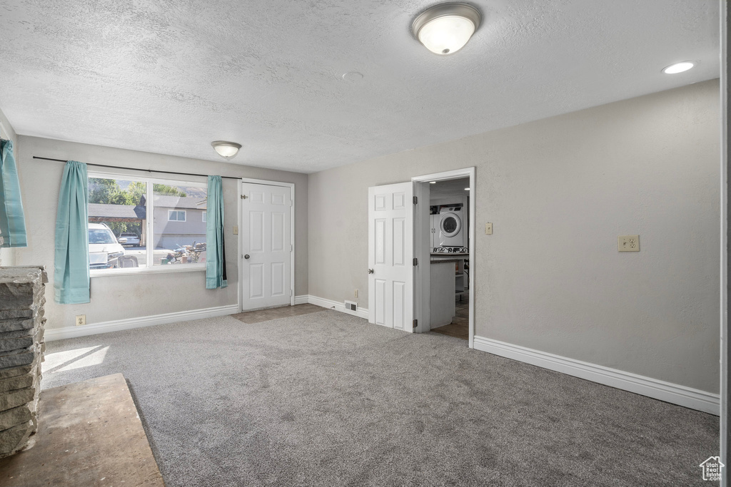 Unfurnished room featuring carpet flooring, a textured ceiling, and stacked washer and clothes dryer