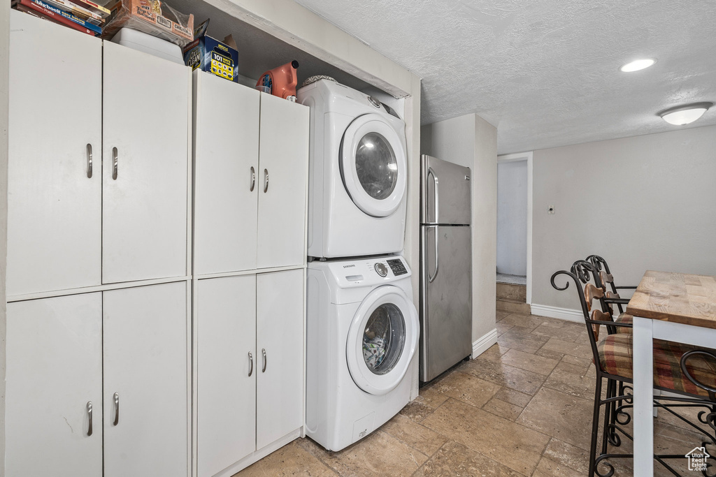 Washroom with light tile patterned floors, stacked washer and clothes dryer, and a textured ceiling