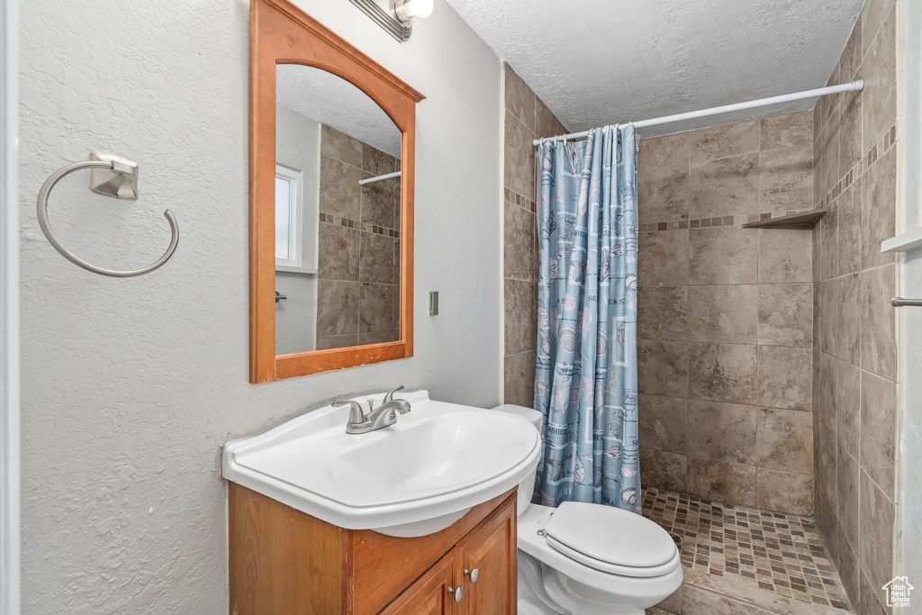 Bathroom with a textured ceiling, toilet, vanity, and walk in shower