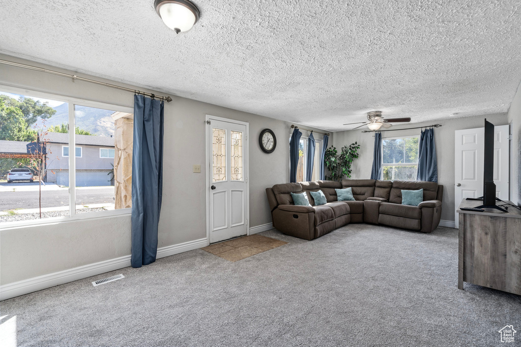 Carpeted living room with ceiling fan and a textured ceiling