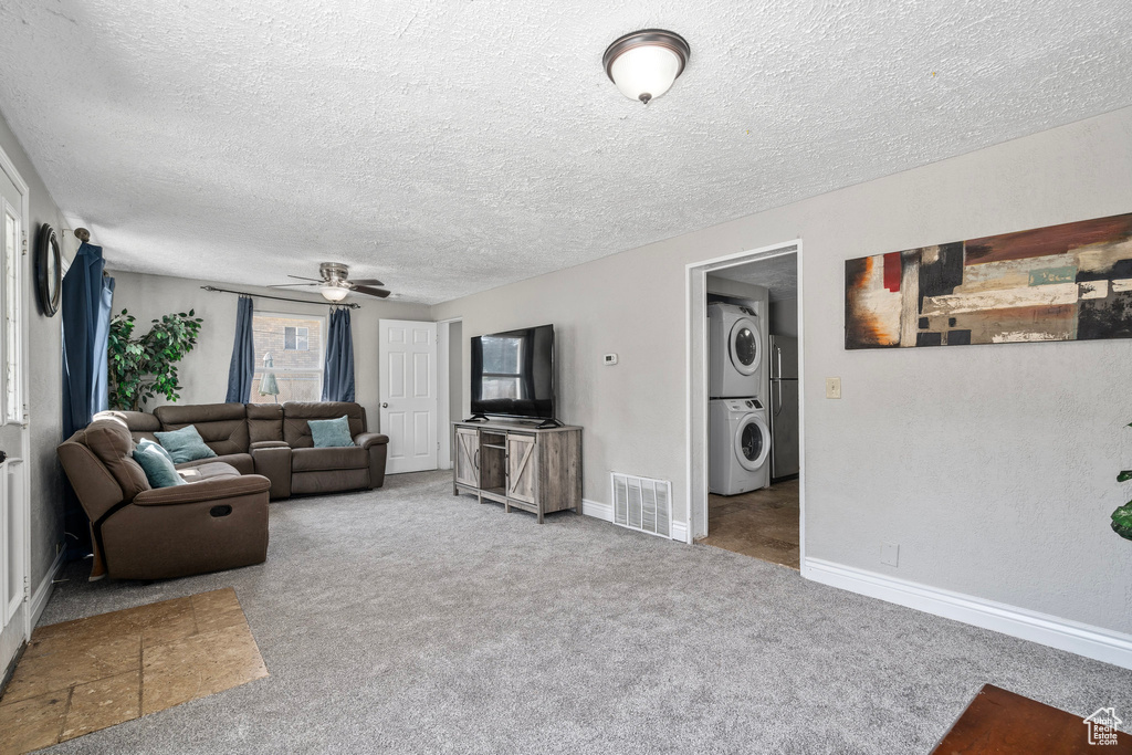 Carpeted living room with ceiling fan, stacked washer / drying machine, and a textured ceiling