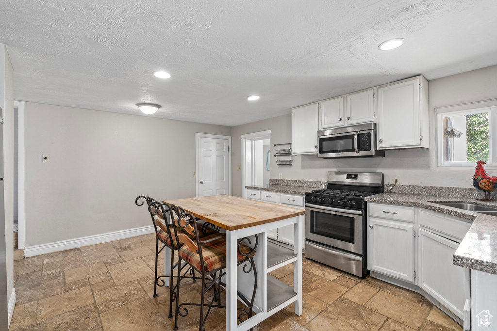 Kitchen with a textured ceiling, stainless steel appliances, light tile patterned flooring, and white cabinets